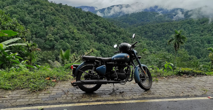 Royal Enfield motorcycle parked on a road surrounded by lush green forest near Vagamon, Kerala